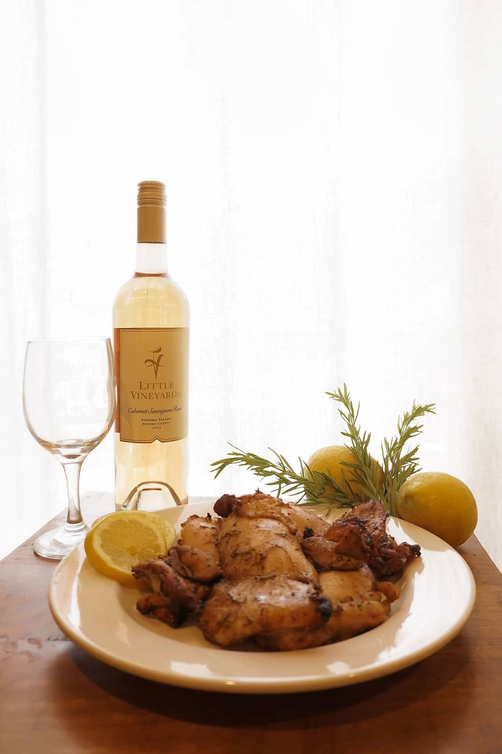 Grilled Herb Chicken on a plate with lemon garnish, wine glass and a bottle of Rose