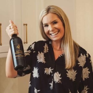 Owner Jessica Little holding and posing with a bottle of wine