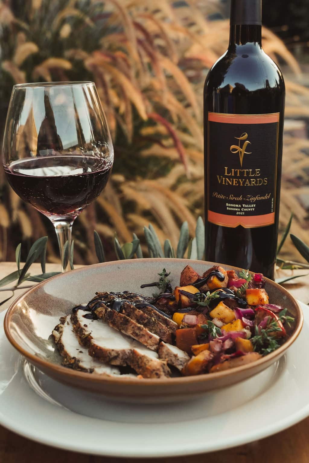 Plated roasted pork with vegetables with a glass of wine and a bottle of bottle in a Fall setting