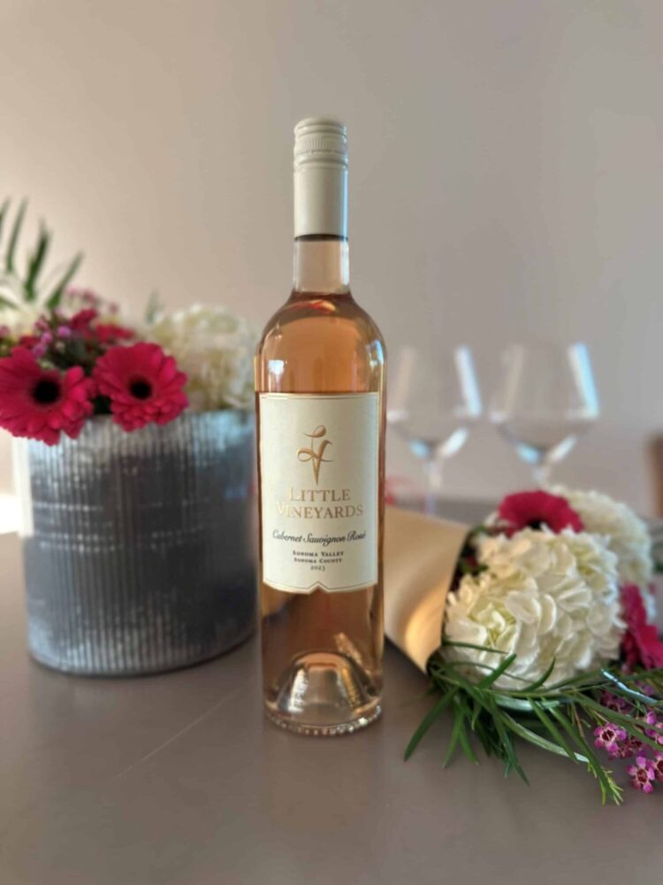 Bottle of Rose with wine glasses and flowers in the background